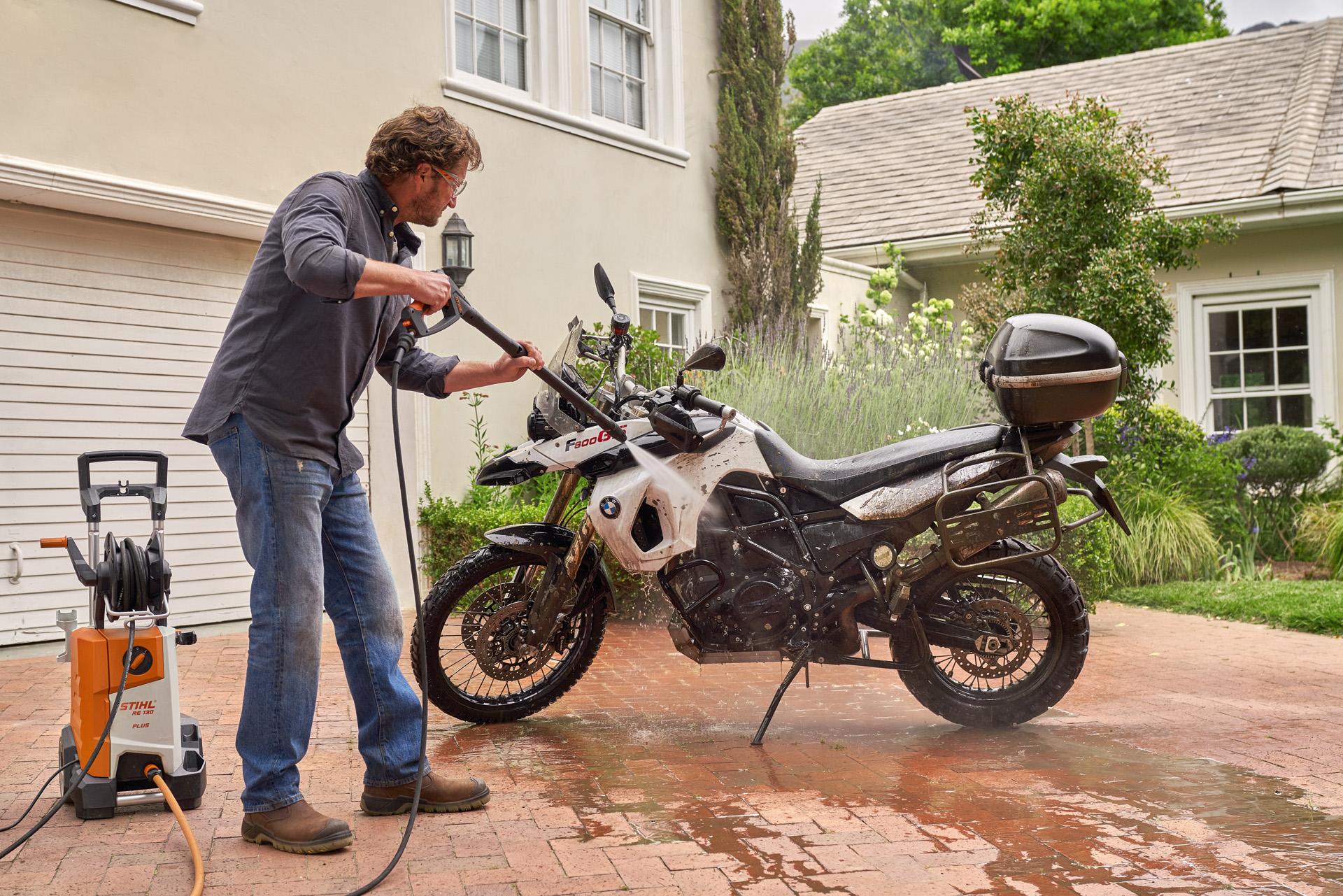 Ένας άνδρας καθαρίζει τη μοτοσικλέτα του μπροστά από το σπίτι με ένα πλυστικό υψηλής πίεσης STIHL RE 130 plus