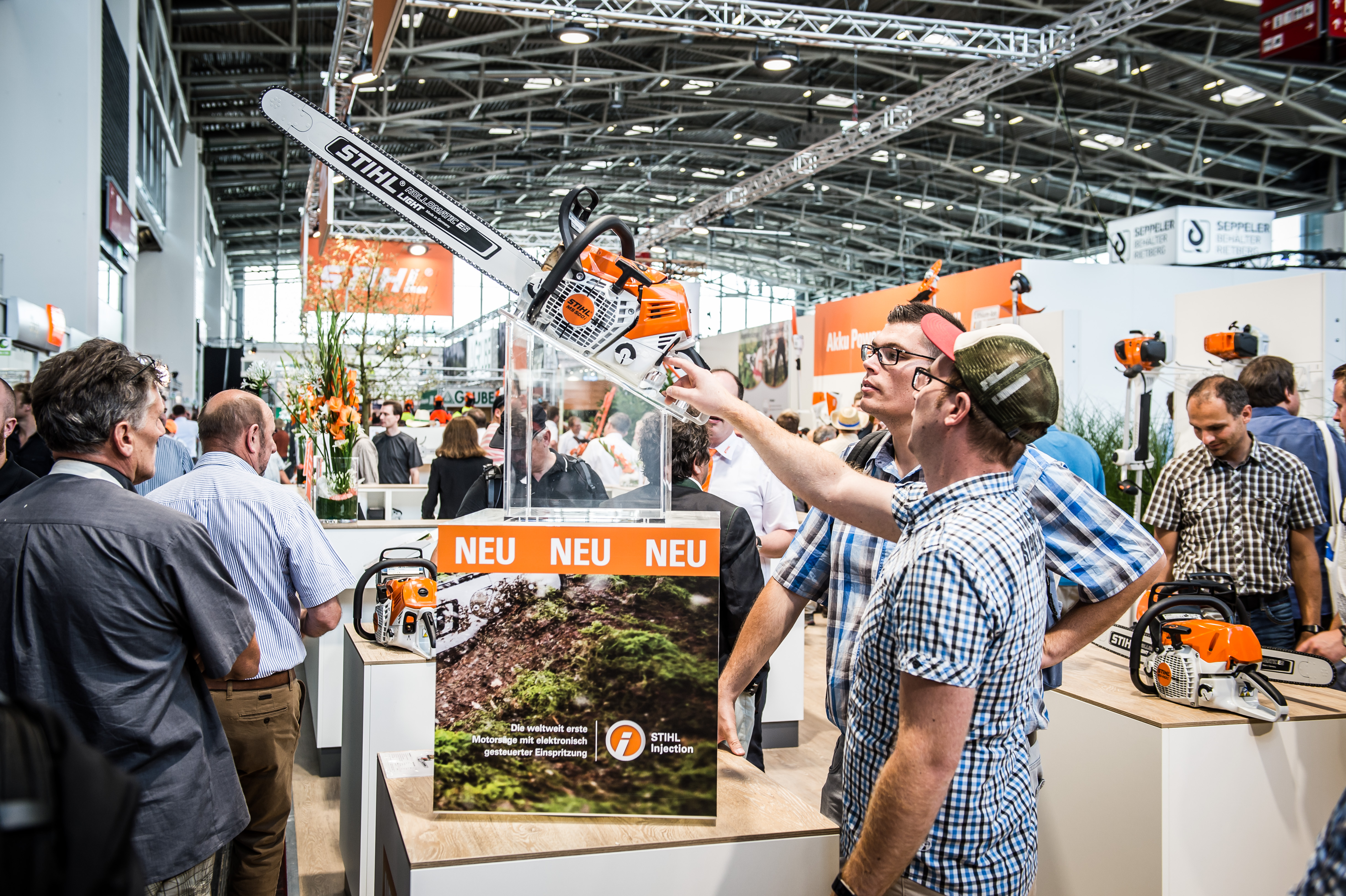 Besucher des STIHL Messestandes schauen sich Produktneuheiten an, darunter eine STIHL Motorsäge 